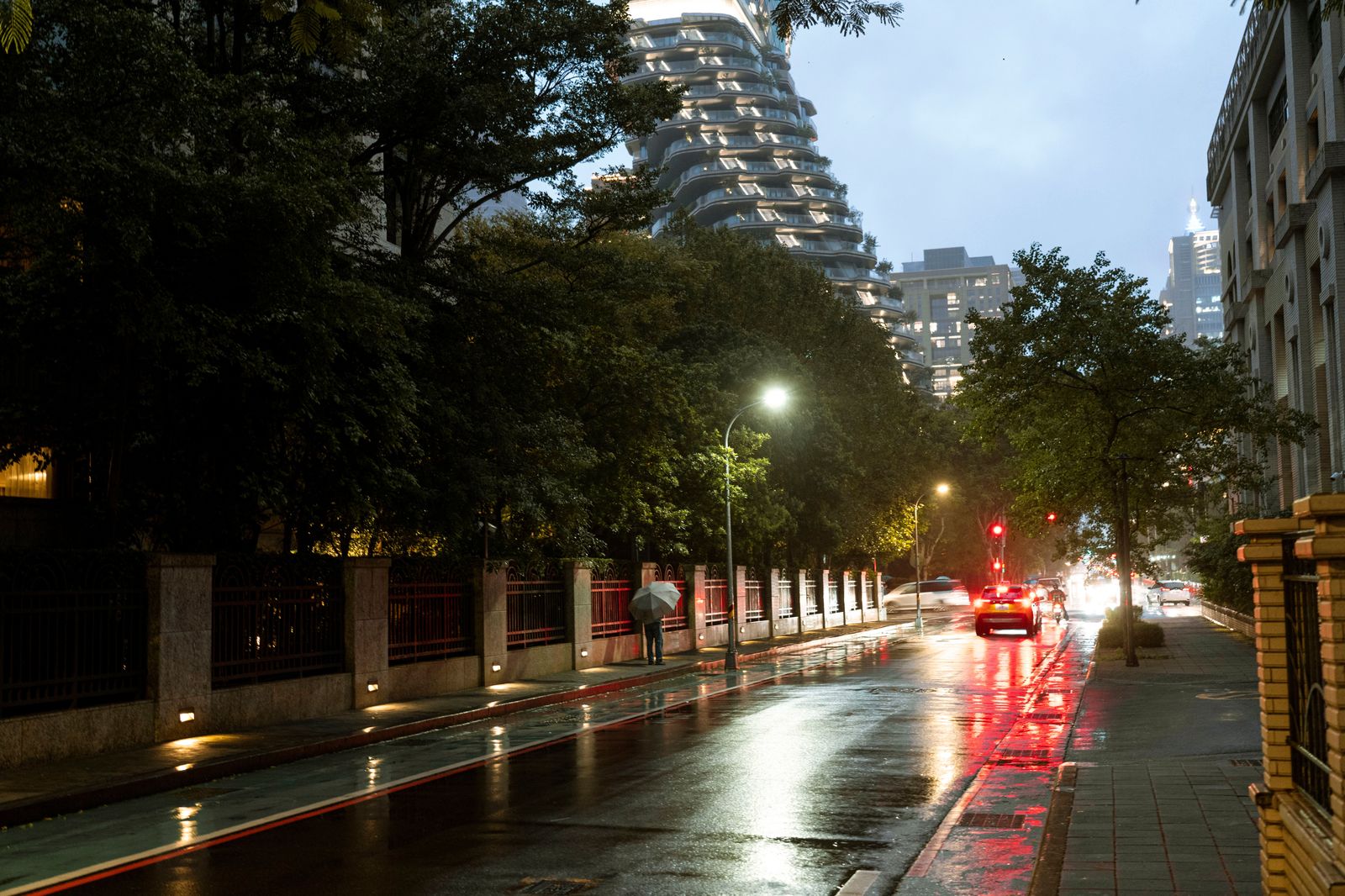 A rainy downtown street in the evening with people under umbrellas