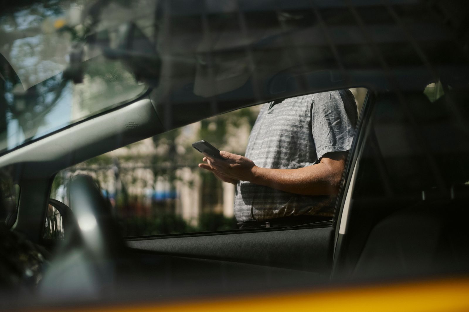 Chauffeur checking a text message beside a black car while waiting for a client