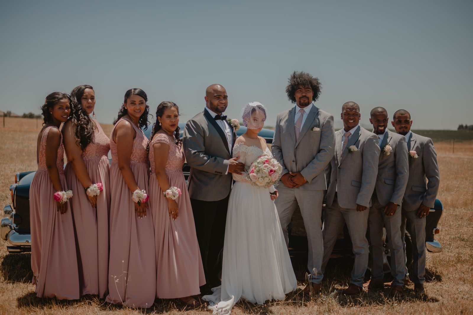 A wedding party gathered beside a stretch limousine for photos