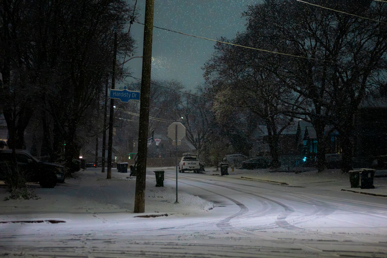 Car driving slowly down a snowy street lined with Christmas lights