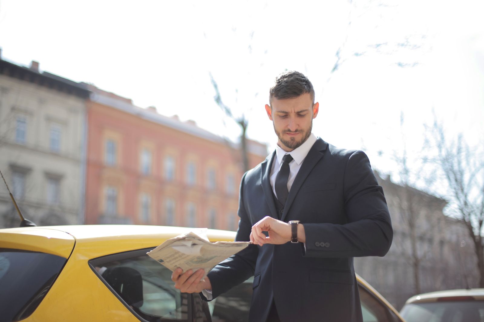 A chauffeur checking the time beside a black car while the client finishes a meeting
