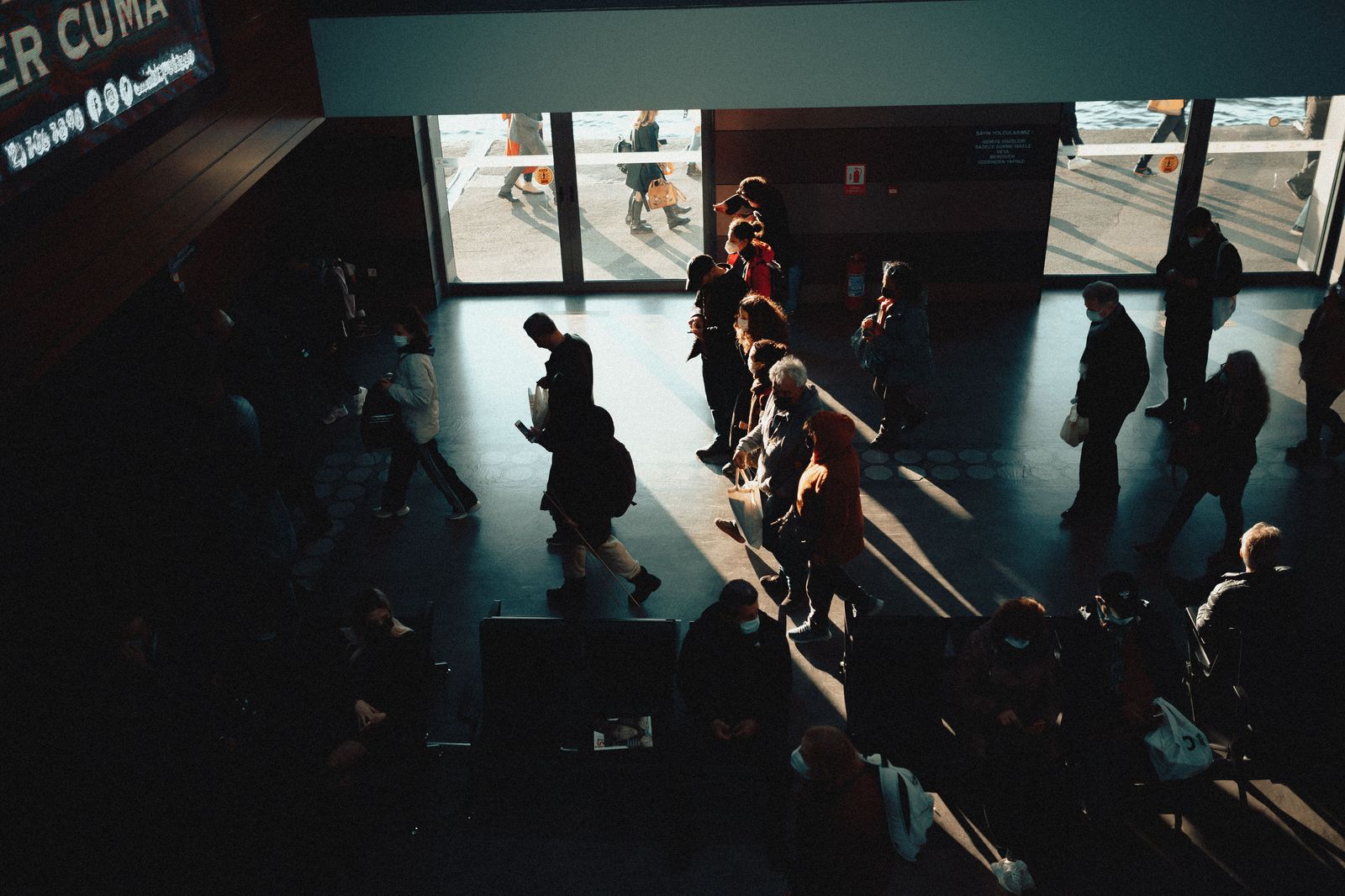 People waiting in an airport arrivals hall; meet and greet with a name board is an optional add-on.