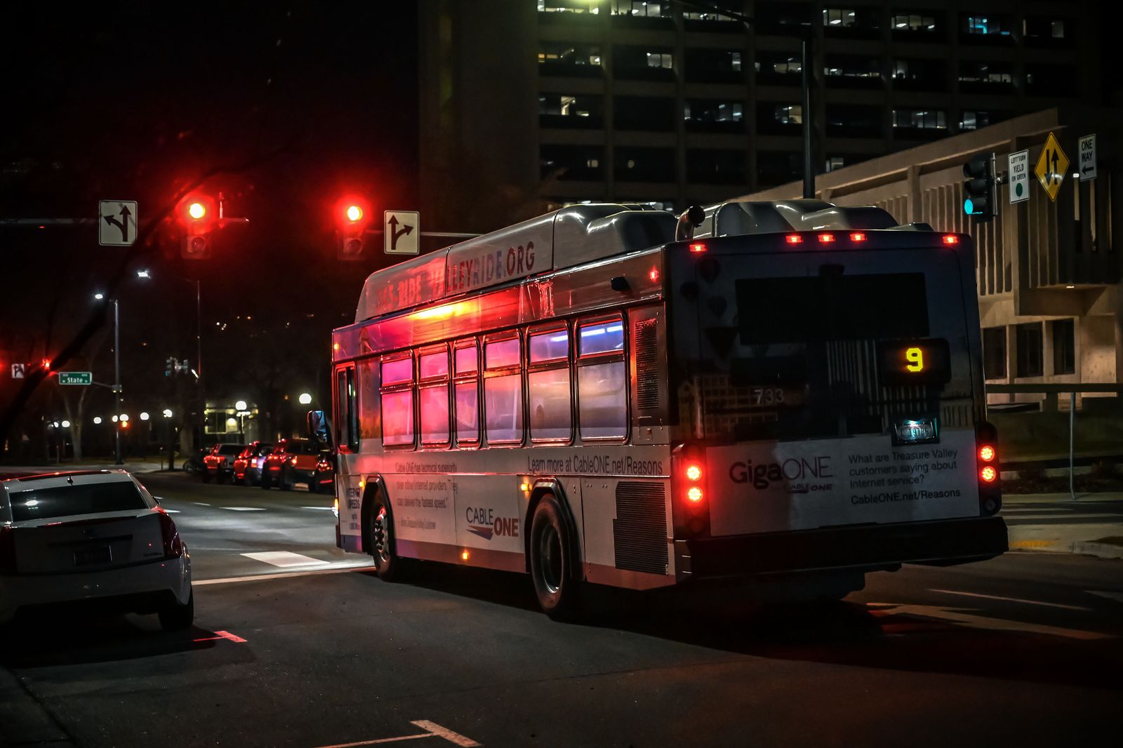 A city bus with its lights on travelling along a road at night
