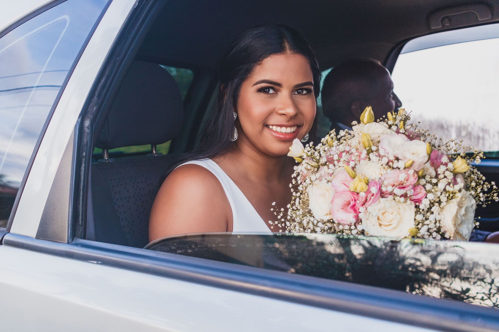 A bride stepping out of a car with the chauffeur holding the door