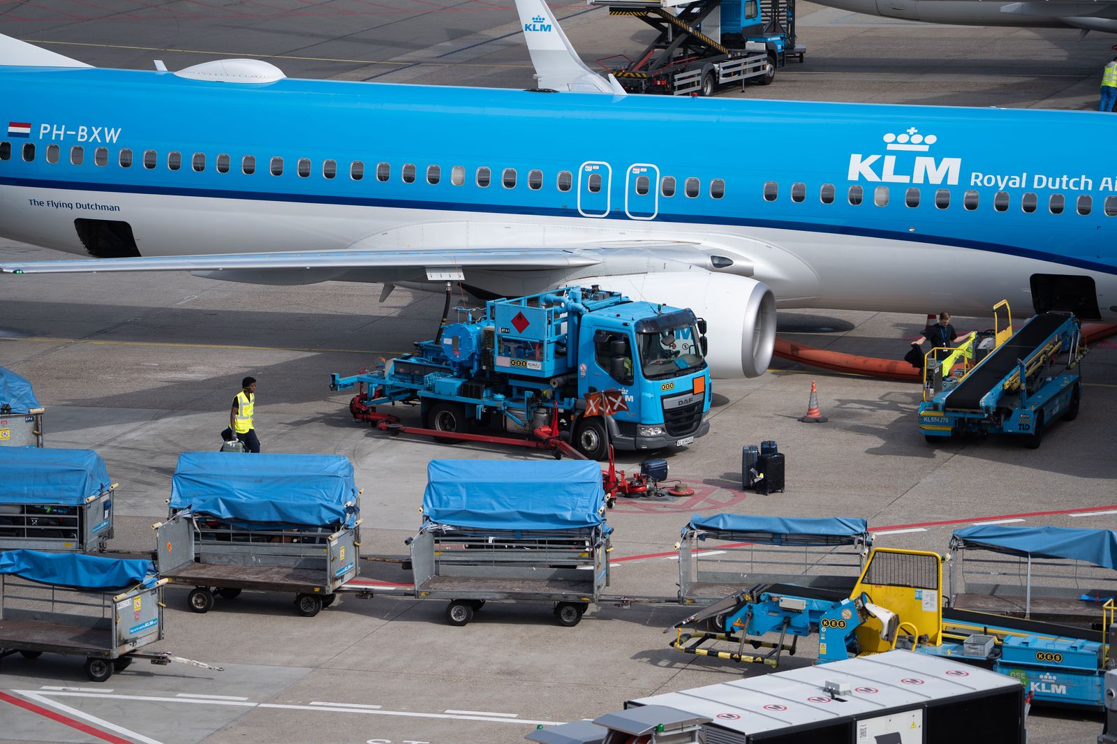 A chauffeur loading suitcases into the trunk of a black car at an airport pickup curb