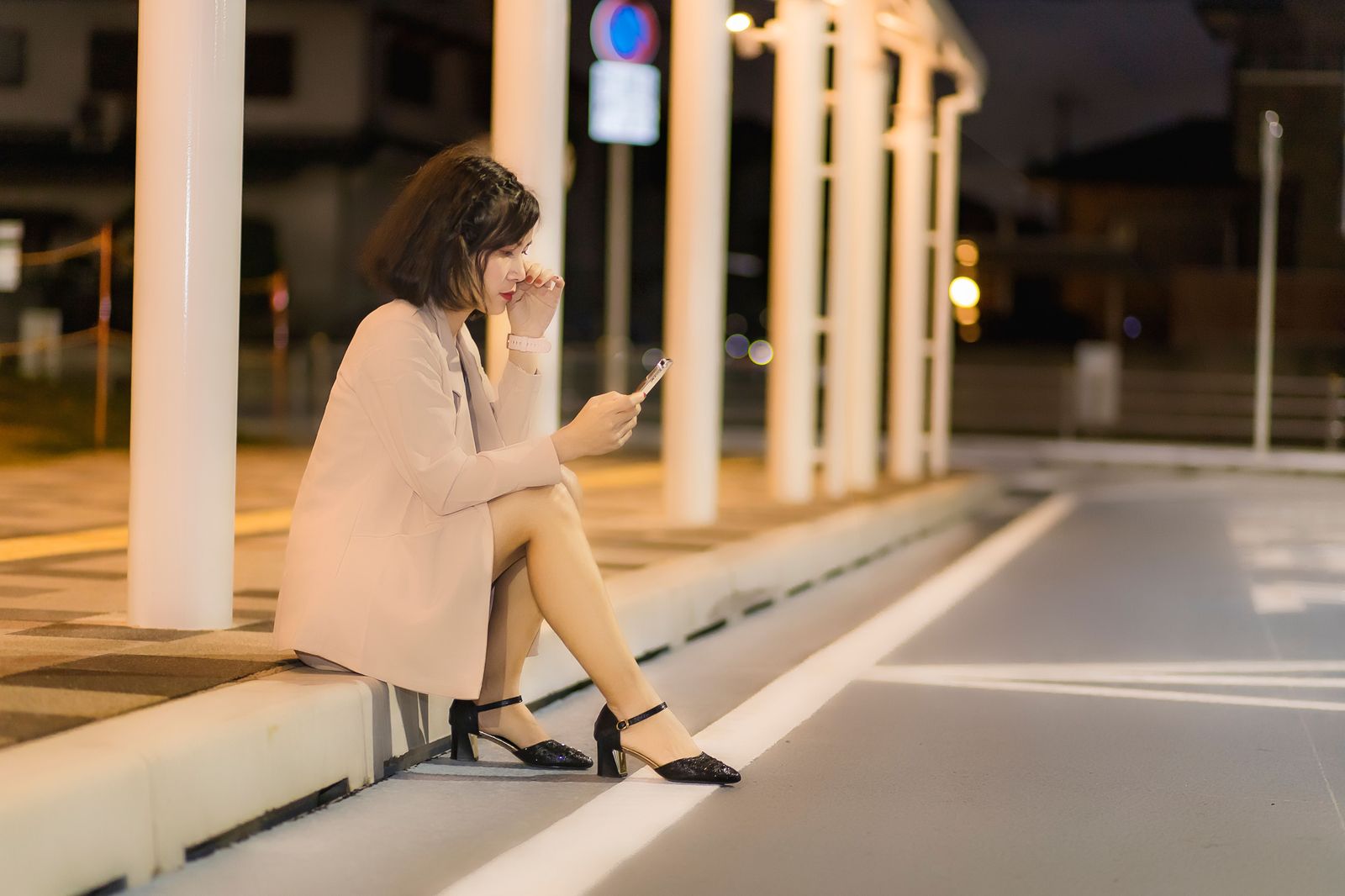A traveller waiting at a curb at night checking a phone for a ride