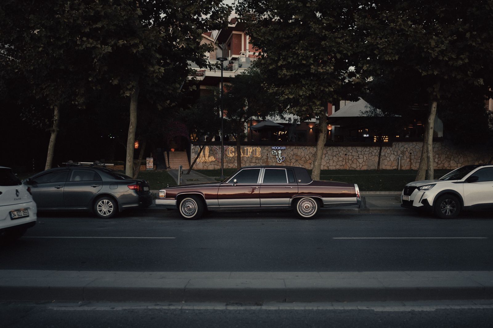 A black sedan pulling up to a downtown curb in the evening