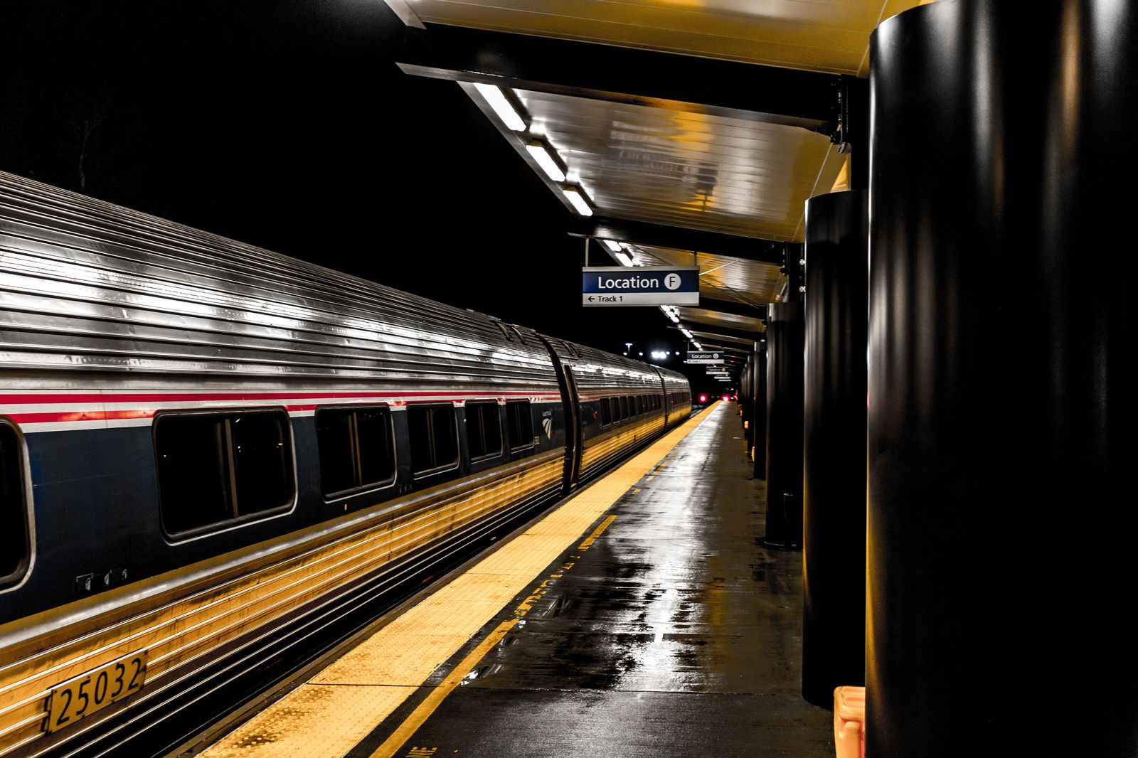 A black car waiting outside a train station at night with its lights on