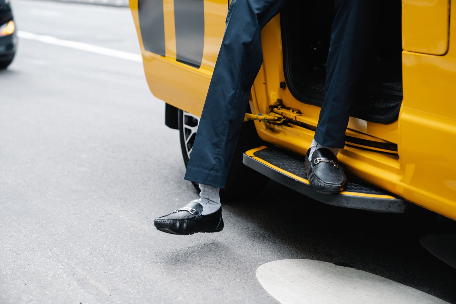 An older man stepping carefully out of a car at his front door with a chauffeur's help