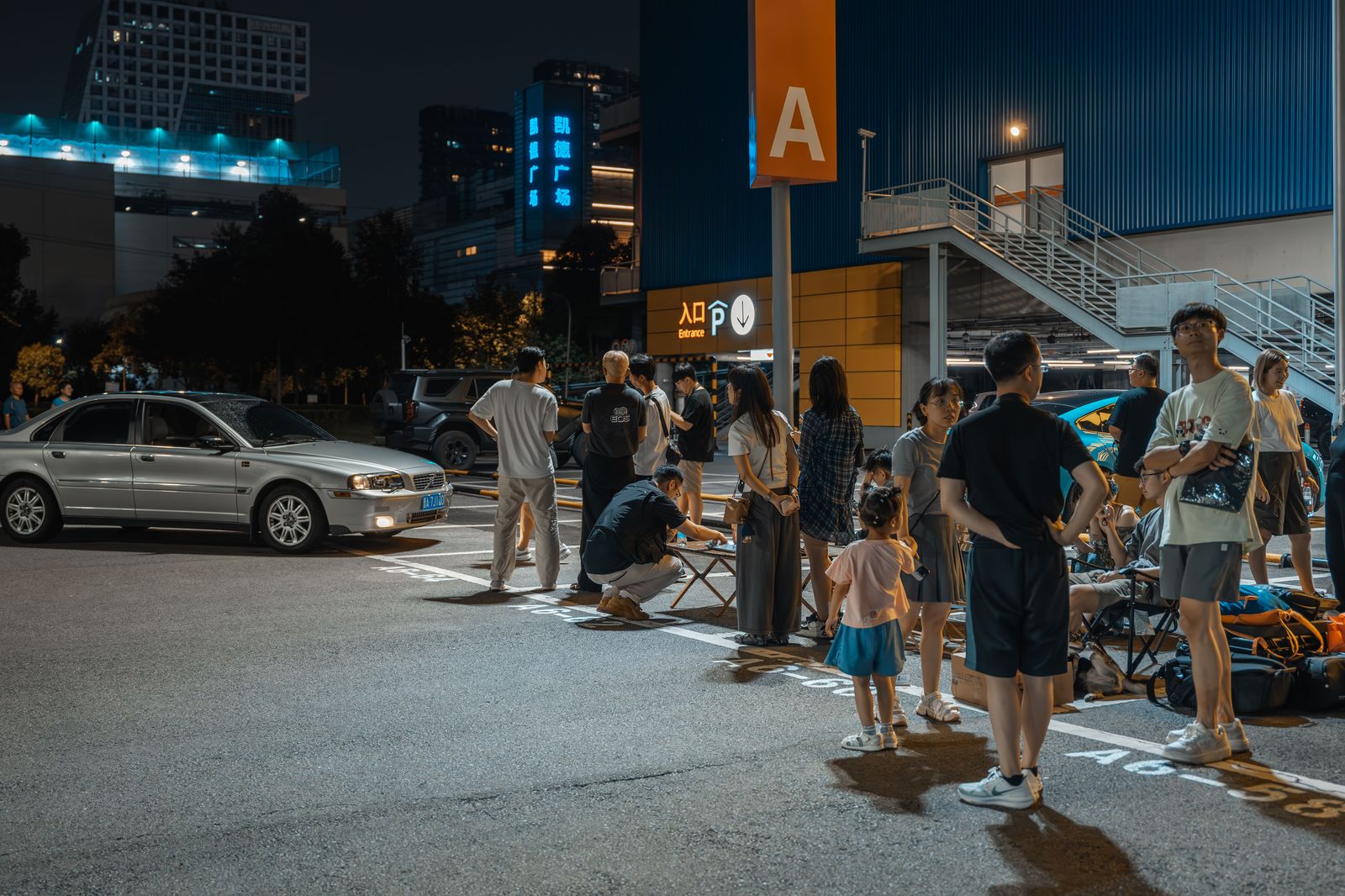 A chauffeur waiting beside a black car outside an airport terminal at night