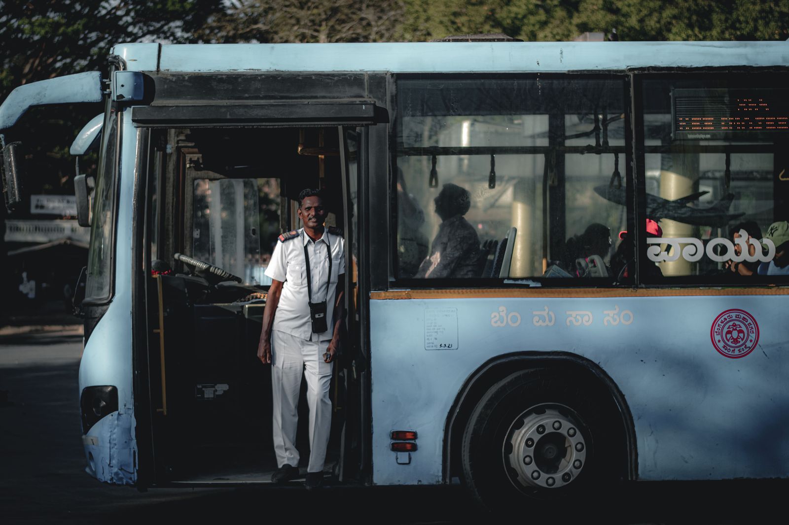 A passenger with a rolling suitcase waiting at a city bus stop