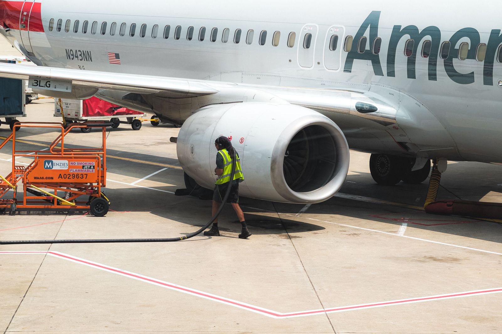 A black sedan stopped at an airport departures curb with the trunk open