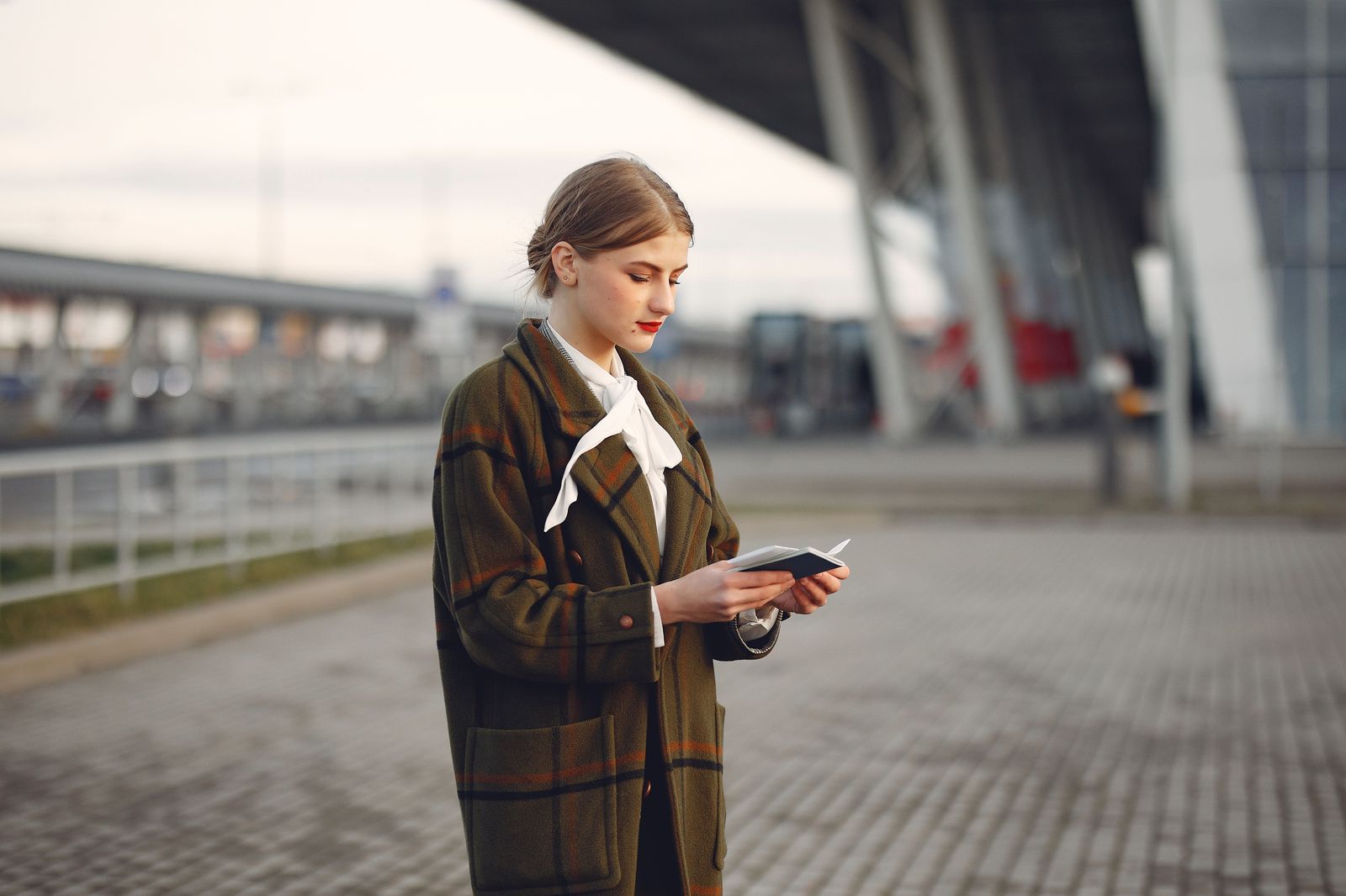 A traveller checking a rideshare app on her phone outside an airport terminal at night
