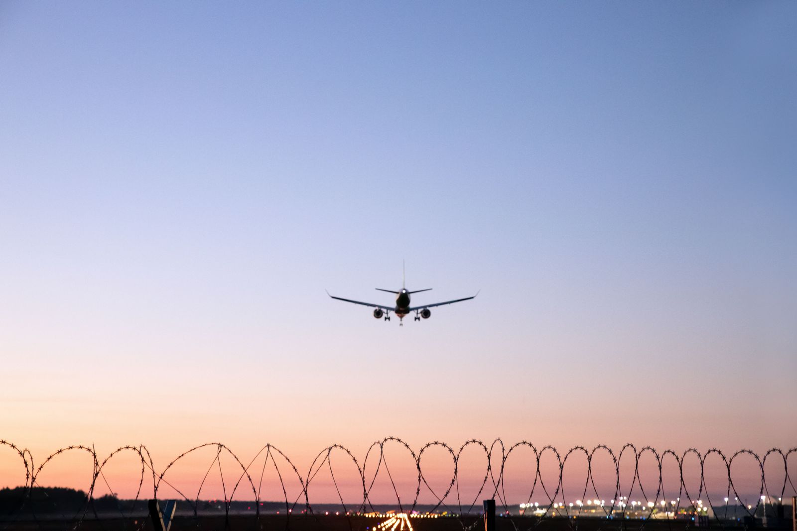 A black sedan waiting at an airport arrivals curb in the evening