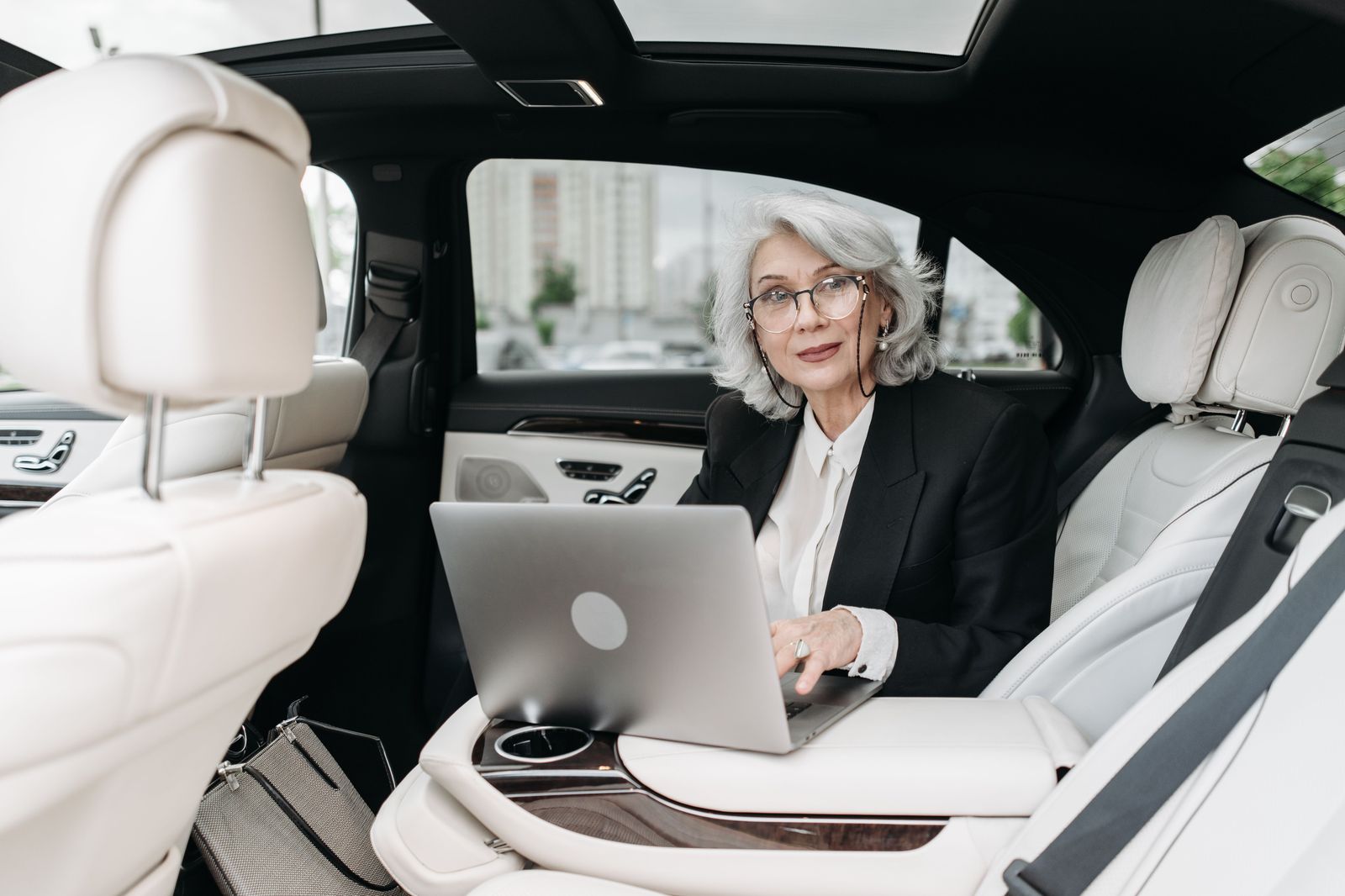A businesswoman working on a laptop in the back seat of a car