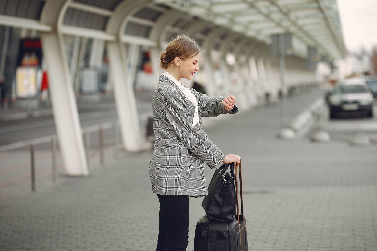 A traveller with a suitcase texting on her phone outside a small airport building