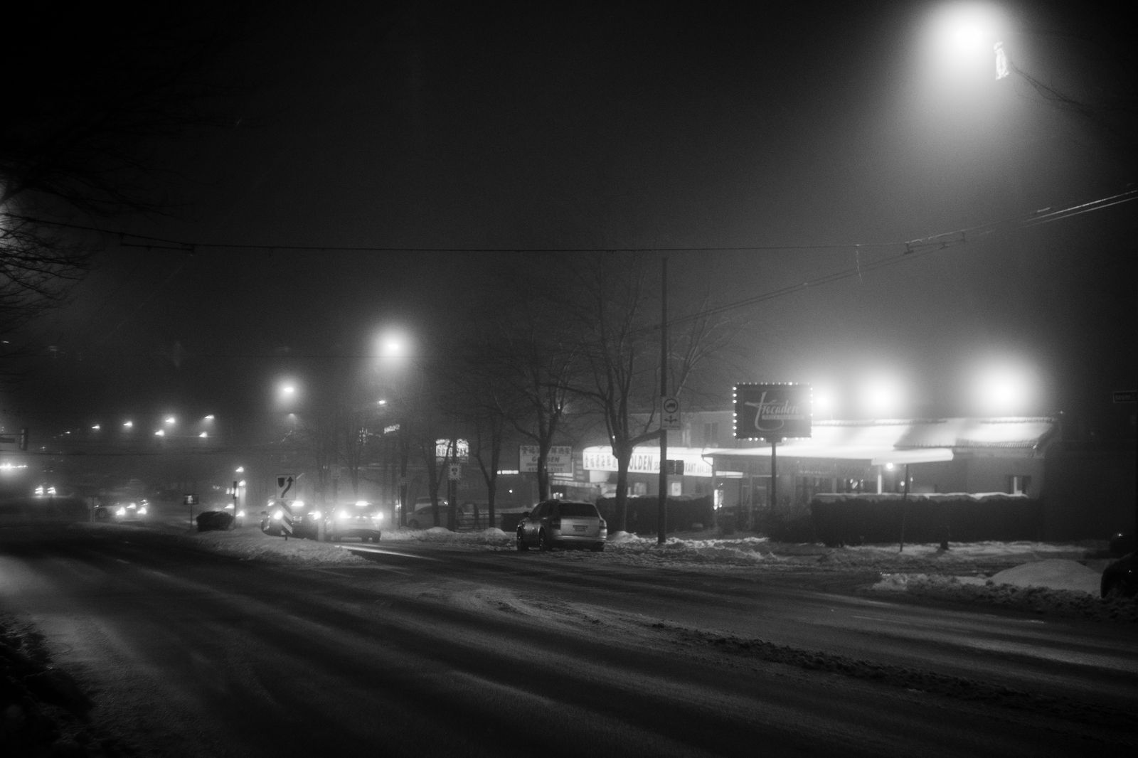 Black sedan driving on a snowy Hamilton street at night during the holidays