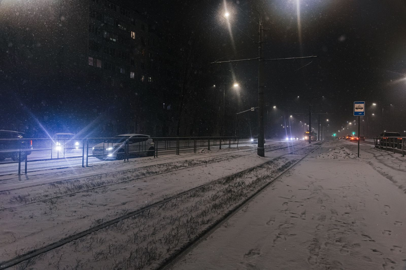 Snowy city street at night with car headlights and falling snow