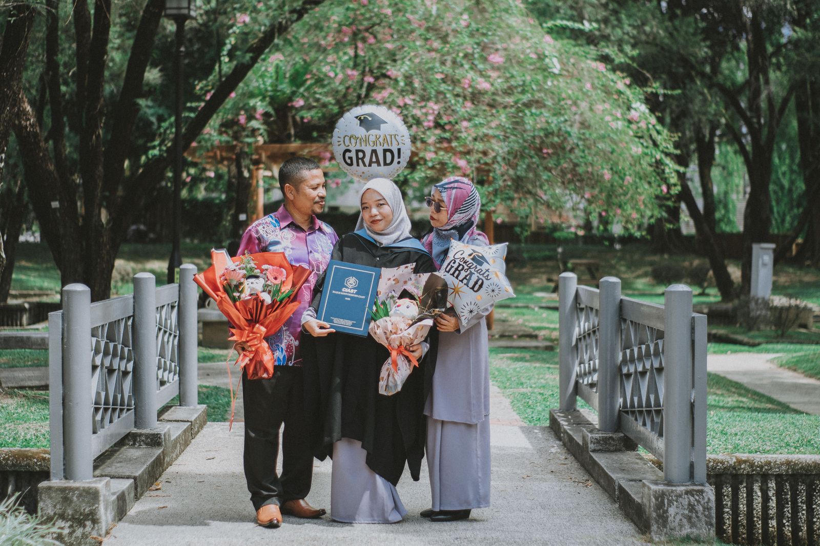 A graduate in a gown with parents holding flowers after the ceremony