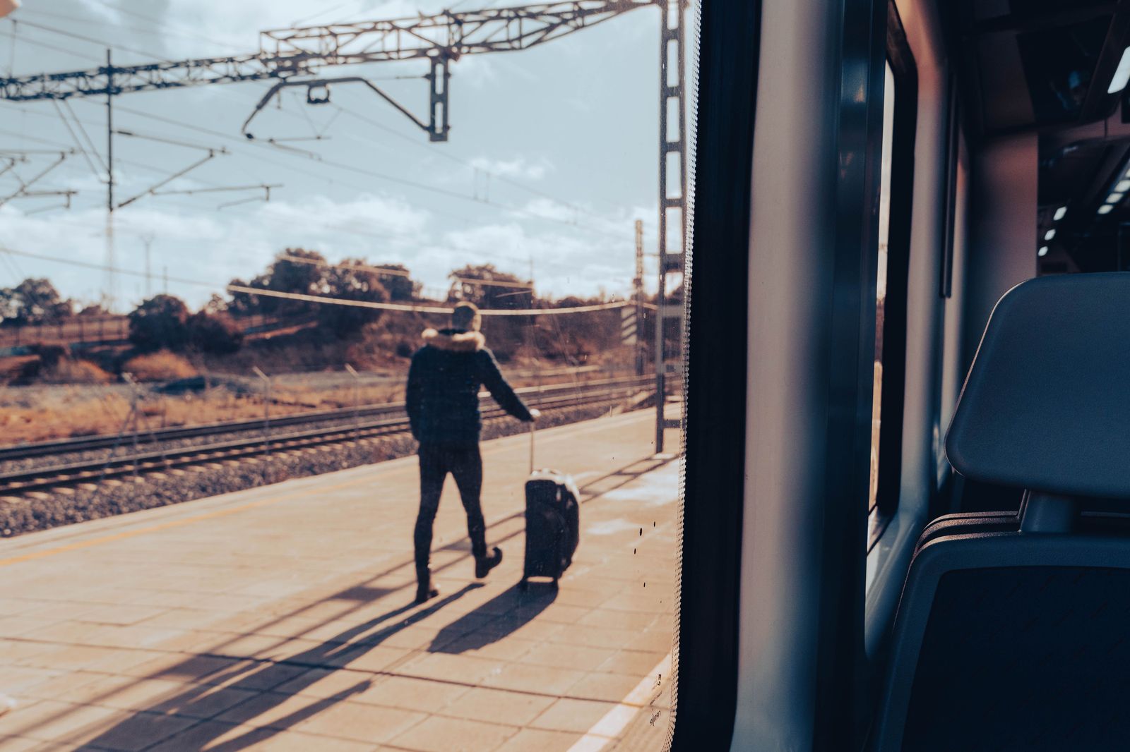A traveller wheeling a suitcase through a train station concourse toward the street exit