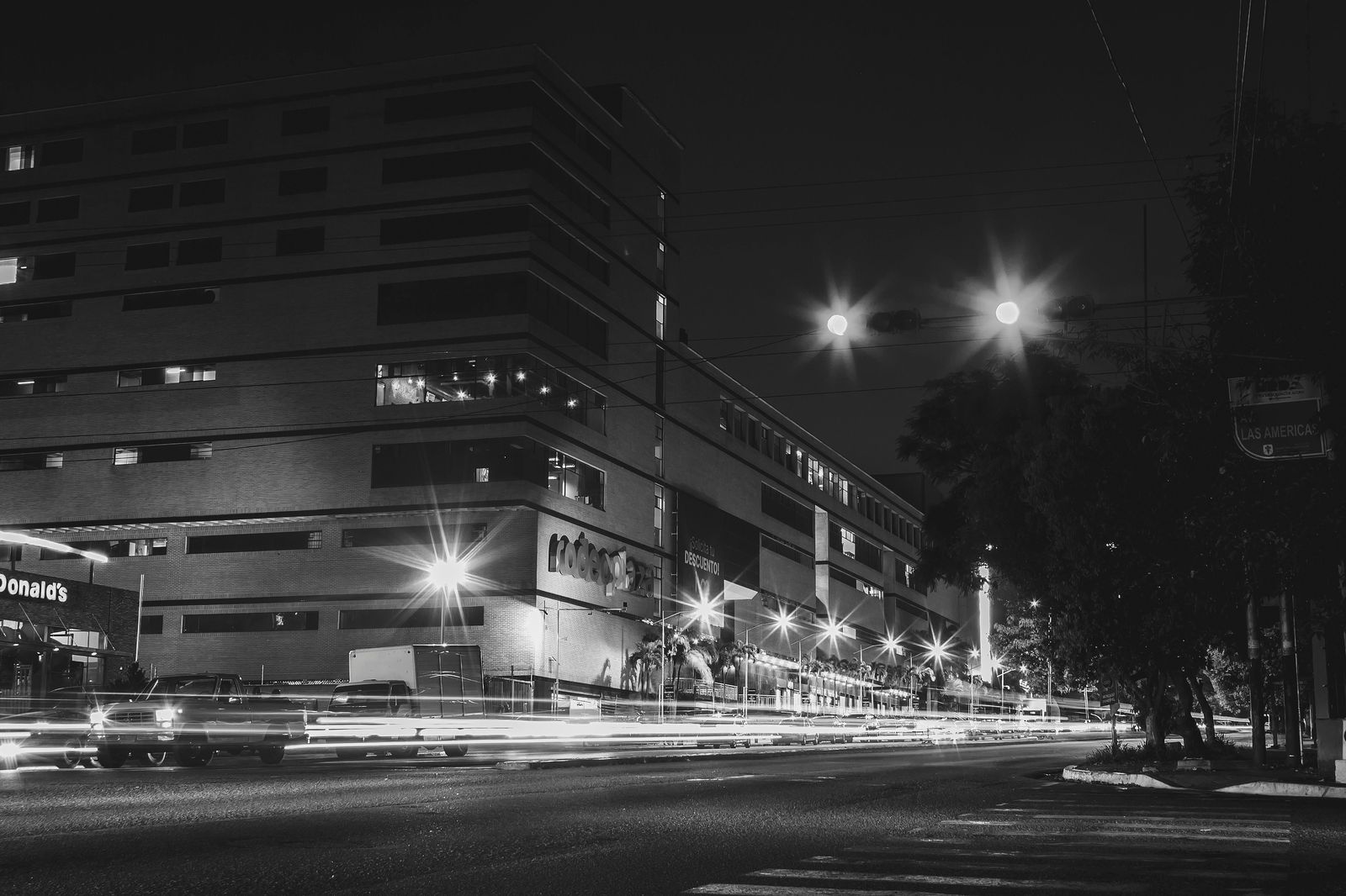 A black sedan waiting on a downtown street at night near a train station