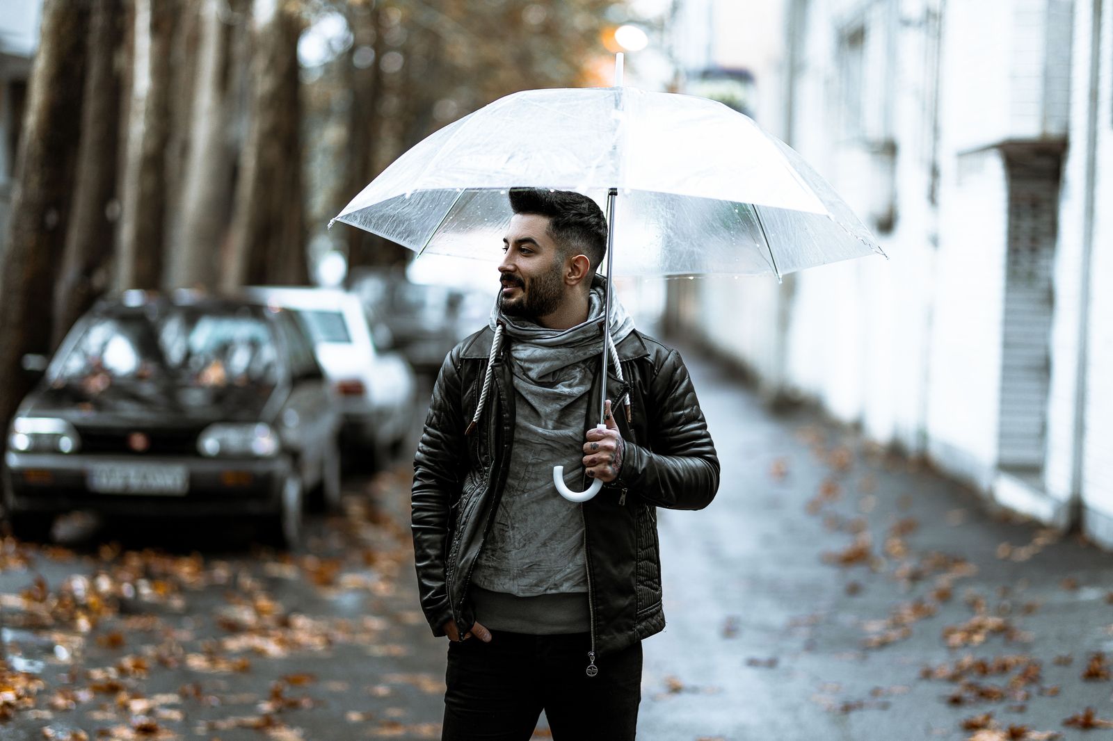 A chauffeur holding an umbrella beside the open door of a black car