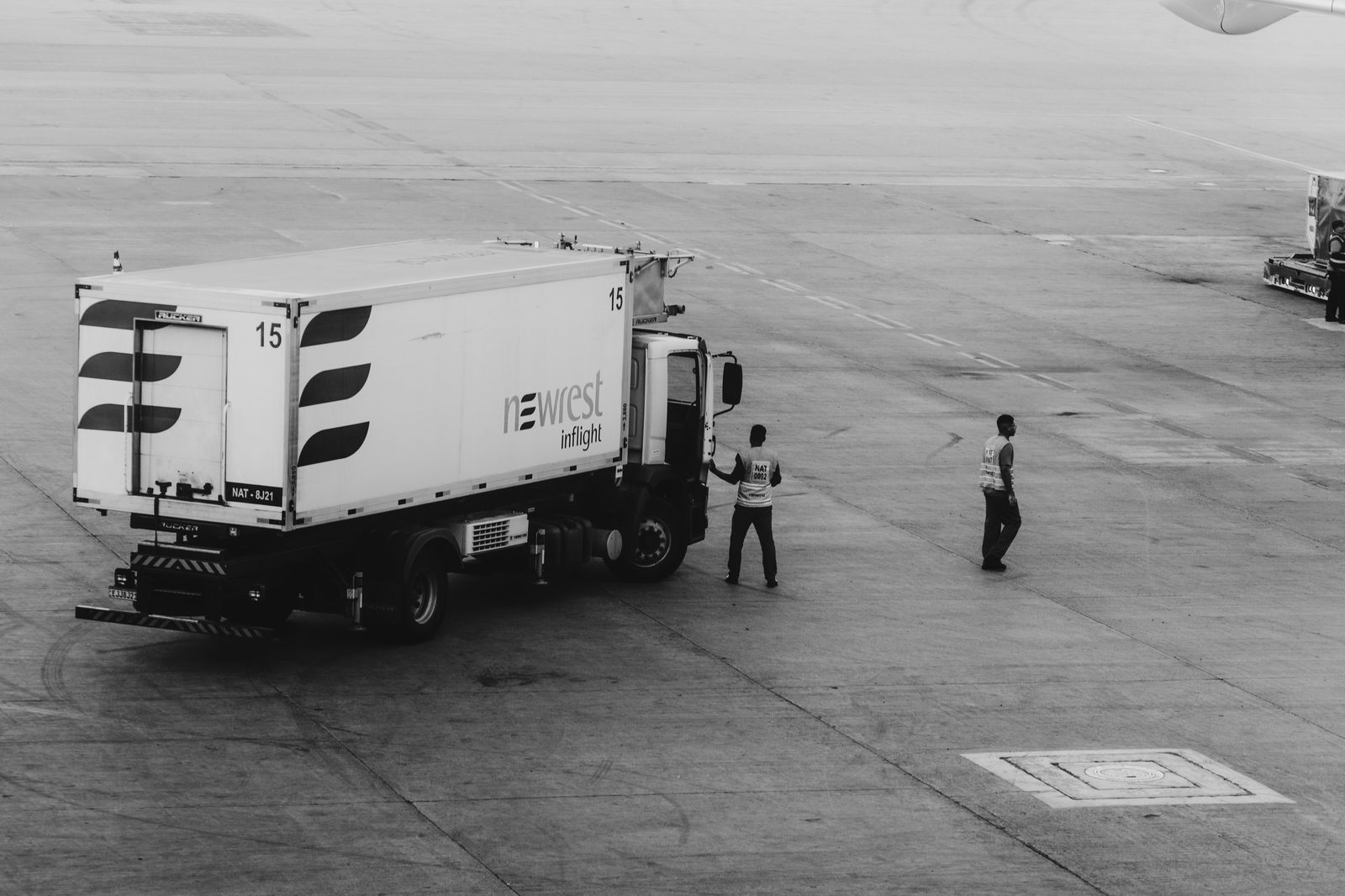 A chauffeur loading a suitcase into the trunk at an airport curb before the drive to Hamilton